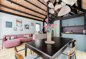 Modernes Wohnzimmer in der Forest villa «De Bosburcht» mit Holzdecke, rosa Sofa und Küche in den Niederlanden.