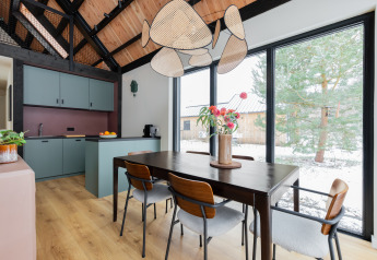 Modern dining area and kitchen in Forest villa De Bosburcht, large windows overlook snowy trees at De Kremmer, Netherlands.