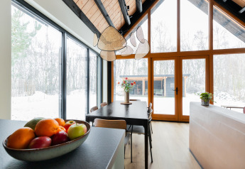 Moderne spisestue med store vinduer og udsigt til sneklædt skov i Forest villa «De Bosburcht», De Kremmer.