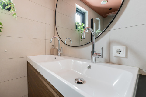 Lavabo moderno con due rubinetti, grande specchio rotondo e finestra presso la Forest villa «De Bosburcht» nei Paesi Bassi.