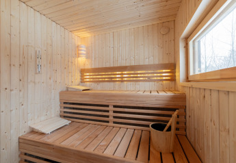 Moderne houten sauna met bank, emmer en raam in Forest villa «De Bosburcht» bij De Kremmer, Nederland.