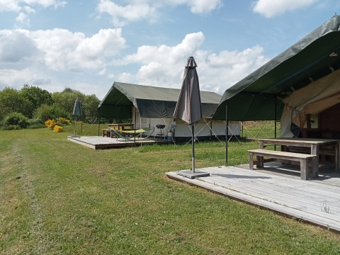Safari-Zelte auf dem Campingplatz La Perle in Frankreich mit Holzterrassen, Sonnenschirmen und Natur.