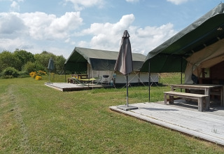 Tentes safari au camping La Perle en France, avec terrasses en bois, parasols et verdure autour.