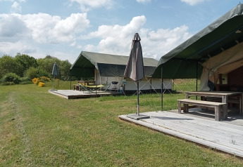 Safari tents at Campsite La Perle in France featuring wooden decks, umbrellas, and lush green scenery.