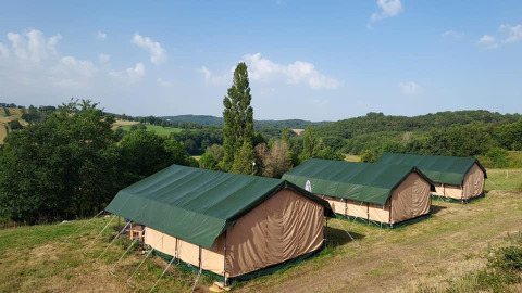 Tentes safari au Camping La Perle en France, installées sur une colline verdoyante avec une vue sur la campagne.