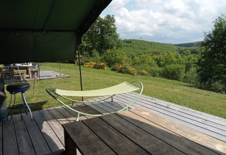Vue depuis la terrasse d’une tente safari au Camping La Perle en France, sur des collines vertes et des fleurs.