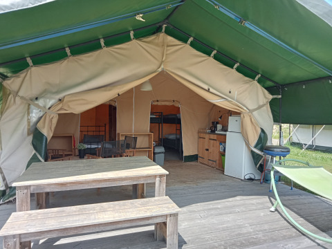 Tente safari au camping La Perle en France avec table en bois, hamac et kitchenette à l'intérieur.