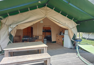 Tente safari au camping La Perle en France avec table en bois, hamac et kitchenette à l'intérieur.