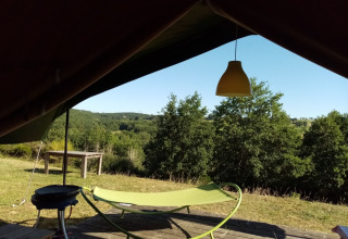 Vue depuis la Safari Tent du Camping La Perle en France, avec hamac, barbecue et collines verdoyantes.