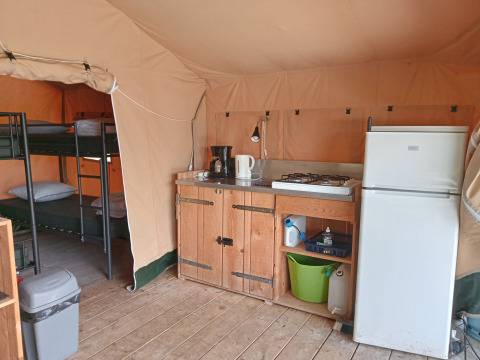 Intérieur de la Safari Tent au camping La Perle en France montrant cuisine, réfrigérateur et lits superposés.