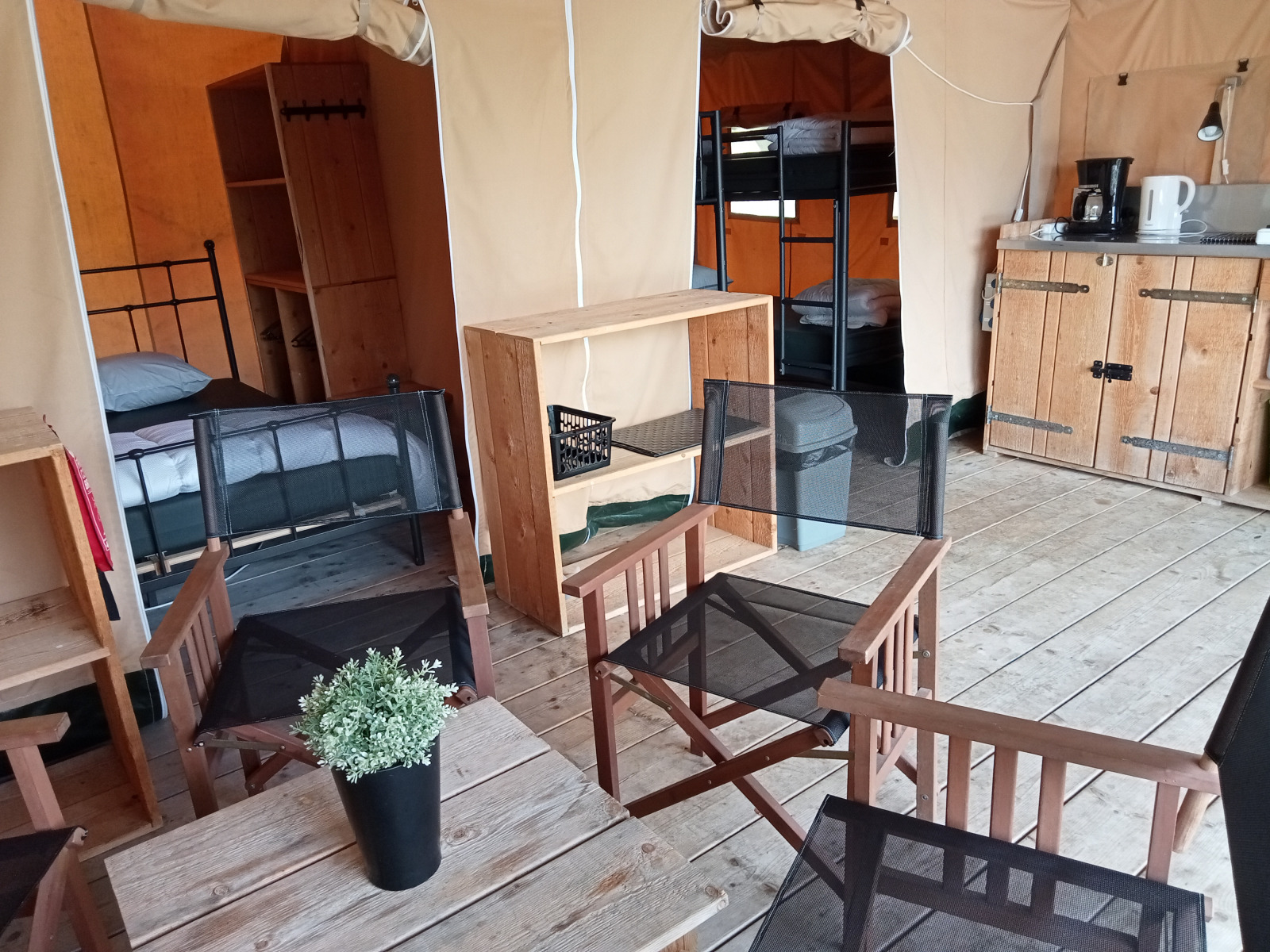 Binnenkant van een safaritent op Camping La Perle in Frankrijk met bedden, stoelen en een kitchenette.