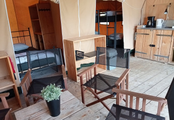Interior view of a safari tent at Campsite La Perle in France featuring beds, chairs, and a kitchenette.