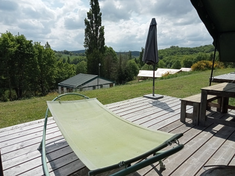 Deck view from Safari Tent at Campsite La Perle in France, featuring a lounge chair and green scenery.