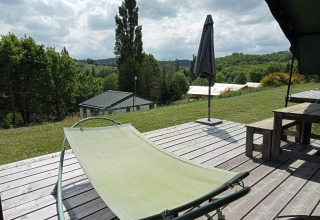 Sonnenterrasse mit Liegestuhl an einem Safari-Zelt auf Campingplatz La Perle, Frankreich, mit Hügelblick.