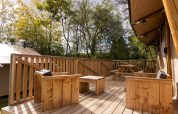 Holzterrasse mit Sitzgelegenheiten und Picknicktisch an der Stardust 40 Family Lodge in Arden Parks, Frankreich.
