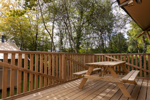 Terraza de madera con mesa de picnic en Stardust 40 Family Lodge, Arden Parks, rodeada de árboles, Francia.