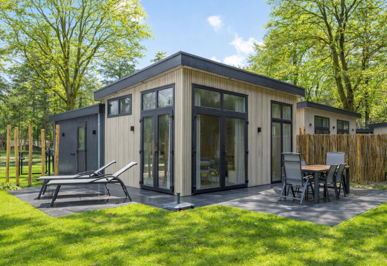 Lodge Veldzicht luminoso con terraza moderna, tumbonas y comedor exterior rodeado de árboles verdes.