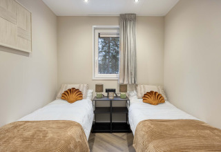 Twee eenpersoonsbedden met gouden kussens in een knusse kamer bij lodge Veldzicht, Forest Park Ede, Nederland.