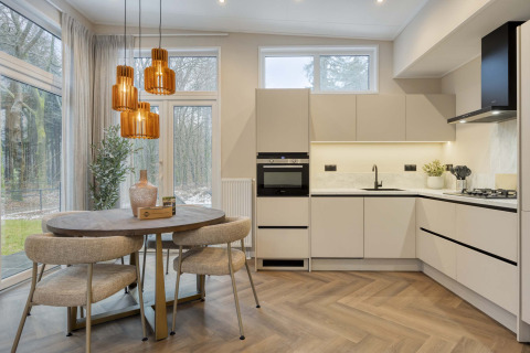 Moderne keuken en eetruimte in lodge ‘Veldzicht’ van Forest Park Ede, Nederland, met grote vensters en sfeerverlichting.