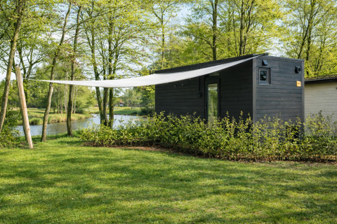 Sort lodge ved floden i grønne omgivelser på Holiday park Mölke, River Mirrorlodge, Holland.