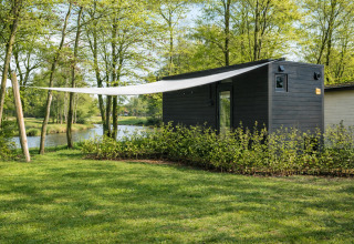 Sort lodge ved floden i grønne omgivelser på Holiday park Mölke, River Mirrorlodge, Holland.