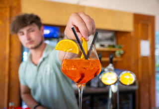 Bartender på feriepark Gooise Heide i Nordholland serverer en Aperol Spritz med appelsinskive og sugerør.