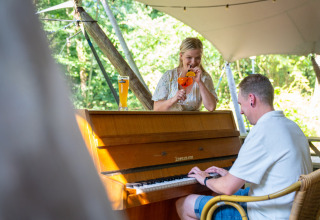To personer nyder musik og drinks ved et klaver udendørs på ferieparken Gooise Heide i Nordholland.