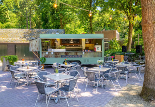 Un food truck avec terrasse extérieure au parc de vacances Gooise Heide, entouré d’arbres en Hollande-Septentrionale.
