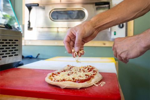 Une personne ajoute du fromage sur une pâte à pizza dans la cuisine du parc de vacances Gooise Heide, Hollande.