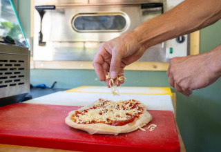 En person forbereder pizza ved at drysse ost på dejen i et køkken på feriestedet Gooise Heide, Holland.