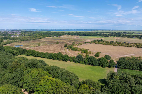 Vue aérienne de la campagne près de Huizen, Pays-Bas, avec des champs, des arbres et des éoliennes lointaines.