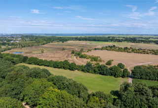 Vista aérea del paisaje cerca de Huizen, Países Bajos, con campos, árboles y turbinas eólicas en la distancia.