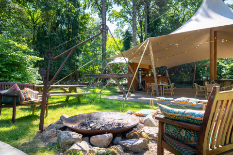 Coin salon extérieur avec feu de camp, coussins colorés et tente au parc de vacances Gooise Heide, Hollande-Septentrionale.
