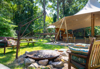 Outdoor lounge with fire pit, colorful cushions, and tent at Gooise Heide holiday park in North Holland.