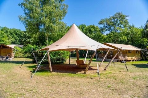 Udendørs teltstruktur, glampinghytter og grønne træer under en klar blå himmel i Gooise Heide, Holland.