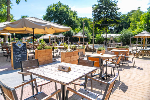 Terrasse d’un café à Gooise Heide, parc de vacances, Hollande-Septentrionale, avec tables en bois et parasols.