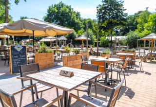 Udendørs caféområde på Gooise Heide feriepark i Nordholland, Holland, med træborde under store parasoller.