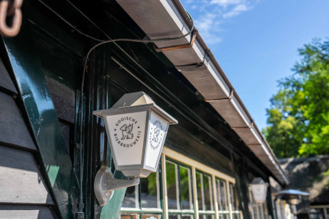 Lámpara de pared exterior con el logo de Gooische Bierbrouwerij en un edificio del parque vacacional Gooise Heide.