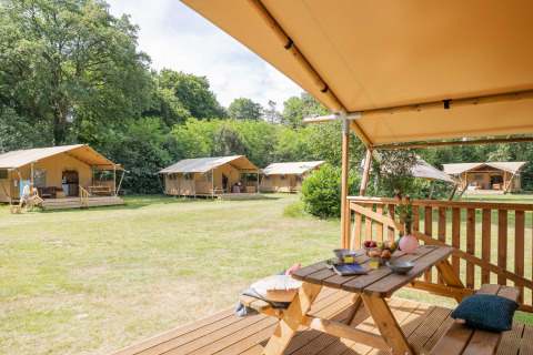 Safari tents at Gooise Heide holiday park in North-Holland, Netherlands, with wooden picnic tables outdoors.