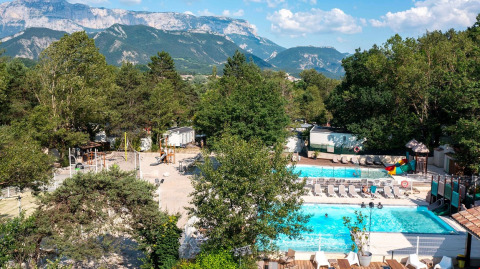 Vista panoramica su Flower Camping la Pinède con piscina, area giochi e montagne in Auvergne-Rhône-Alpes.