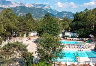 Blick auf Flower Camping la Pinède mit Pool, Kinderspielplatz und Bergpanorama in Auvergne-Rhône-Alpes.