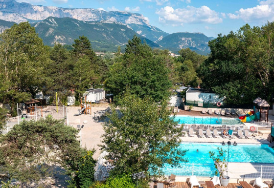 Udsigt over Flower Camping la Pinède med swimmingpool, legeplads og bjerge i baggrunden, Auvergne-Rhône-Alpes.