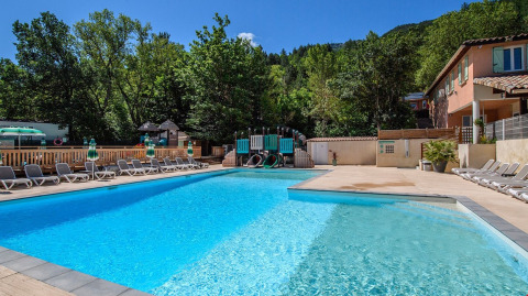 Outdoor swimming pool with lounge chairs and a children’s play area at Flower Camping la Pinède in France.
