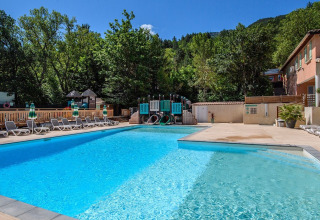 Udendørs swimmingpool med liggestole, legeplads og træer på Flower Camping la Pinède, Auvergne-Rhône-Alpes.