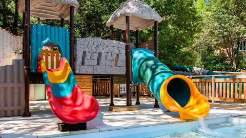Aire de jeux avec toboggans colorés près d'une piscine au Flower Camping la Pinède, Auvergne-Rhône-Alpes, France.