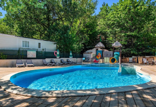 Piscine extérieure avec toboggans et transats entourée d’arbres au Flower Camping la Pinède en France.