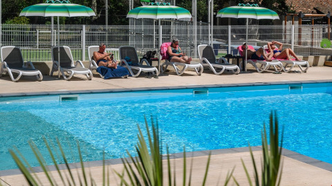 People relaxing on lounge chairs under green umbrellas by the pool at Flower Camping la Pinède in France.