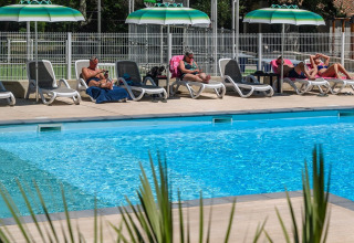Des personnes se détendent sur des transats sous des parasols verts près de la piscine au Flower Camping la Pinède, France.