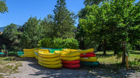 Stacks of colorful kayaks at Flower Camping la Pinède holiday park surrounded by trees in Auvergne-Rhône-Alpes.
