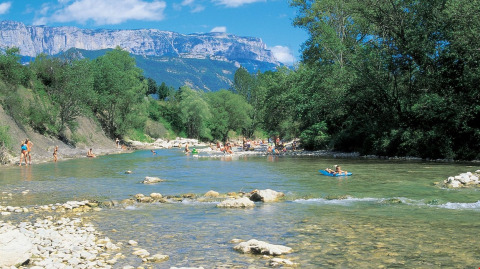 Personas disfrutan del río en Flower Camping la Pinède, con montañas al fondo en Auvergne-Rhône-Alpes, Francia.
